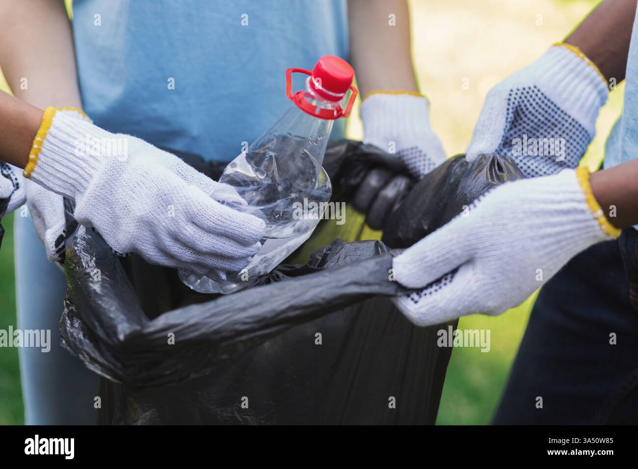 Bénévoles portant des gants en tissu blanc pour ramasser des bouteilles en plastique recyclables dans un sac poubelle à l'extérieur Banque D'Images