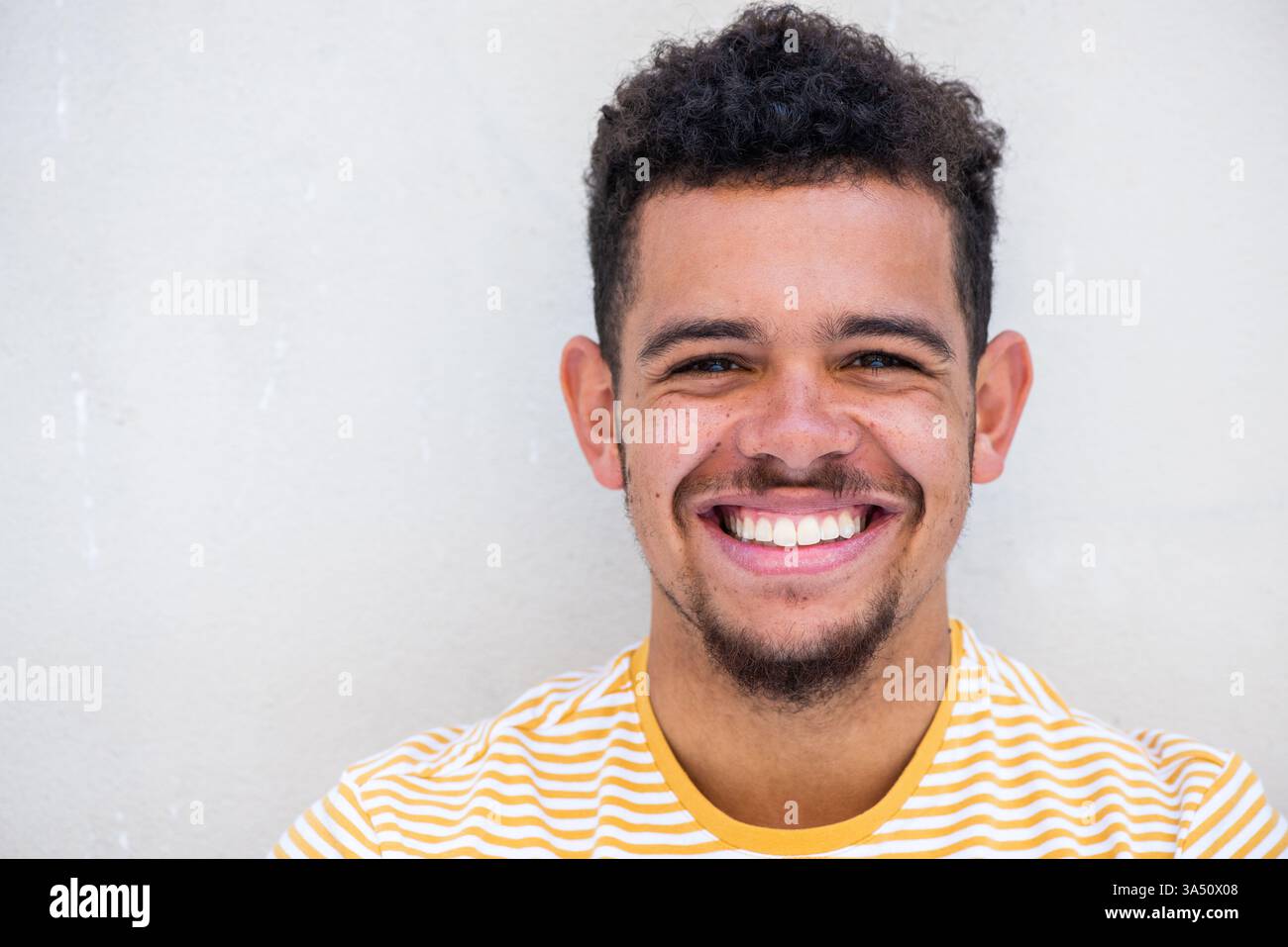 Portrait en gros plan d'un joyeux homme de race mixte avec une barbe sur un fond blanc. Il respire la confiance et l'accessibilité, adapté au style de vie, à la mode et aux thèmes de masculinité moderne. Idéal pour les visuels de marque d'entreprise ou personnelle. Banque D'Images