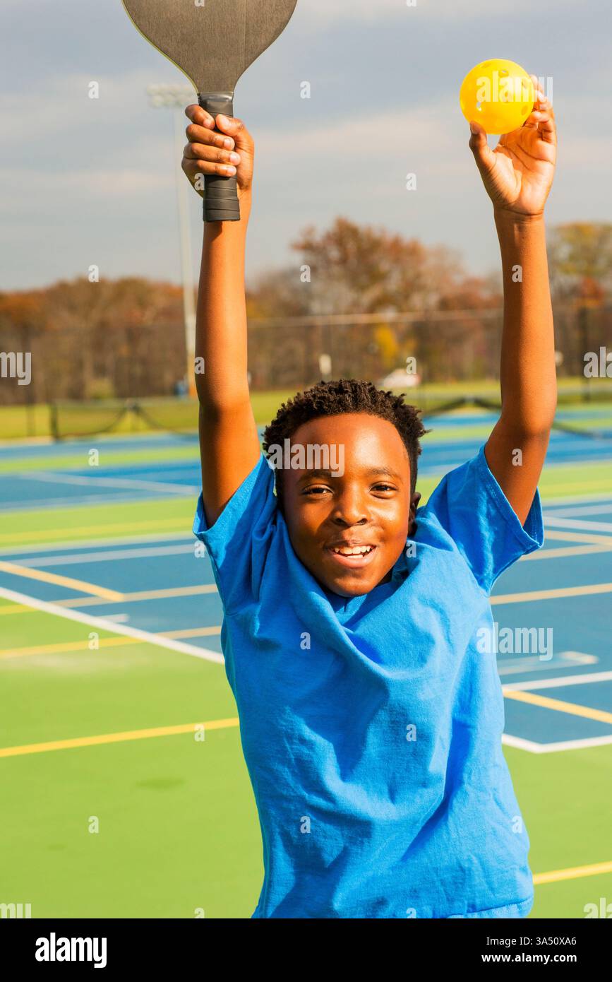 Athlète précoce pratiquant une variété de sports de raquette, y compris le racquetball sur un court. Cette scène sportive jeune fonctionne bien pour le conditionnement physique, les programmes pour les jeunes et les campagnes scolaires. L'énergie occasionnelle et amateur transmet l'apprentissage et l'activité. Banque D'Images