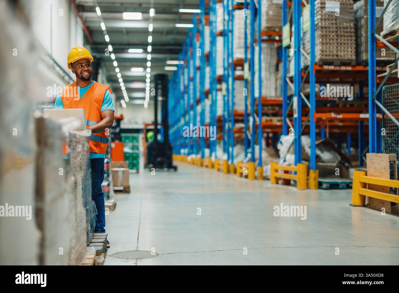Un homme noir ouvrier d'entrepôt se tient parmi des étagères imposantes et utilise un ordinateur portable pour gérer la logistique. La scène souligne comment la technologie stimule l'efficacité de la distribution et de la chaîne d'approvisionnement moderne. Idéal pour le contenu sur les opérations d'entrepôt, la logistique numérique et la technologie professionnelle du lieu de travail. Banque D'Images
