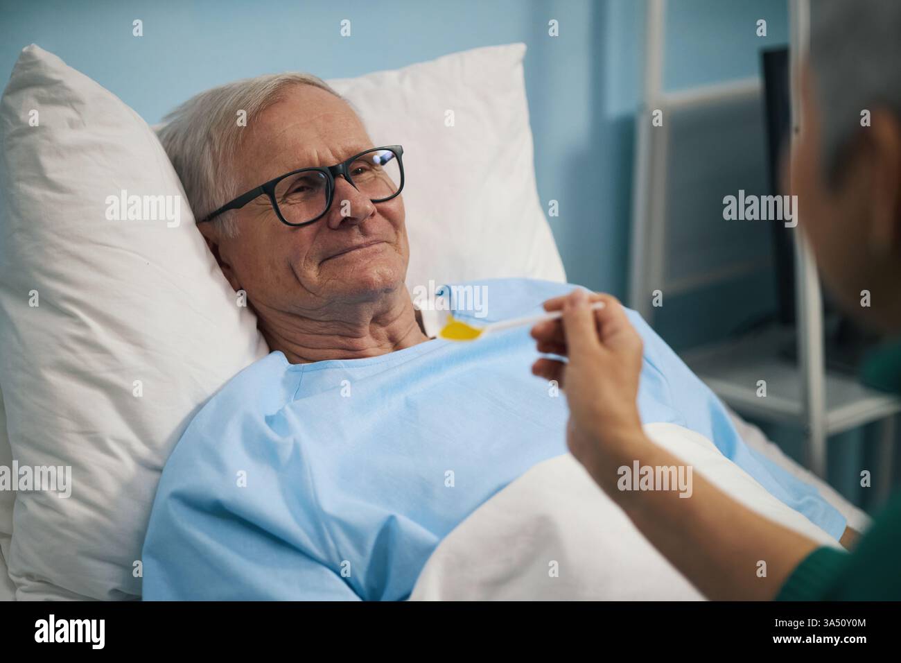 Homme âgé souriant allongé sur le lit dans la salle et souriant à sa femme pendant qu'elle le nourrit Banque D'Images