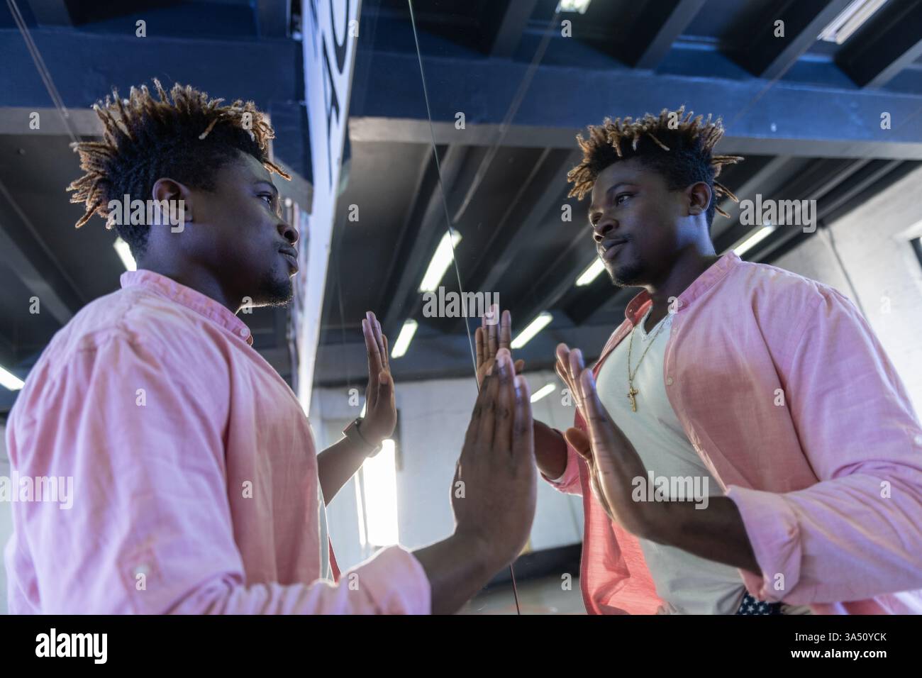 Portrait dynamique d'un Noir dans un studio de danse, regardant son reflet dans le miroir. Vêtu de vêtements sportifs colorés, il respire la confiance et la concentration comme il pratique la chorégraphie. Banque D'Images