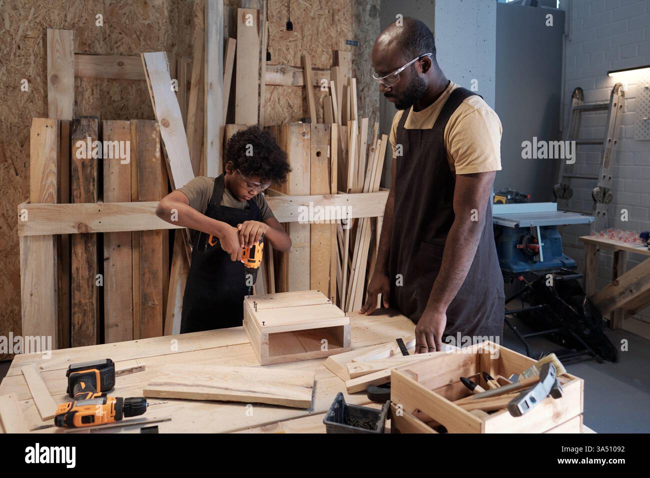 Portrait d'un garçon construisant un nichoir en bois avec son père dans un atelier. Un moment sain de paternité, d'artisanat et de lien familial. Banque D'Images