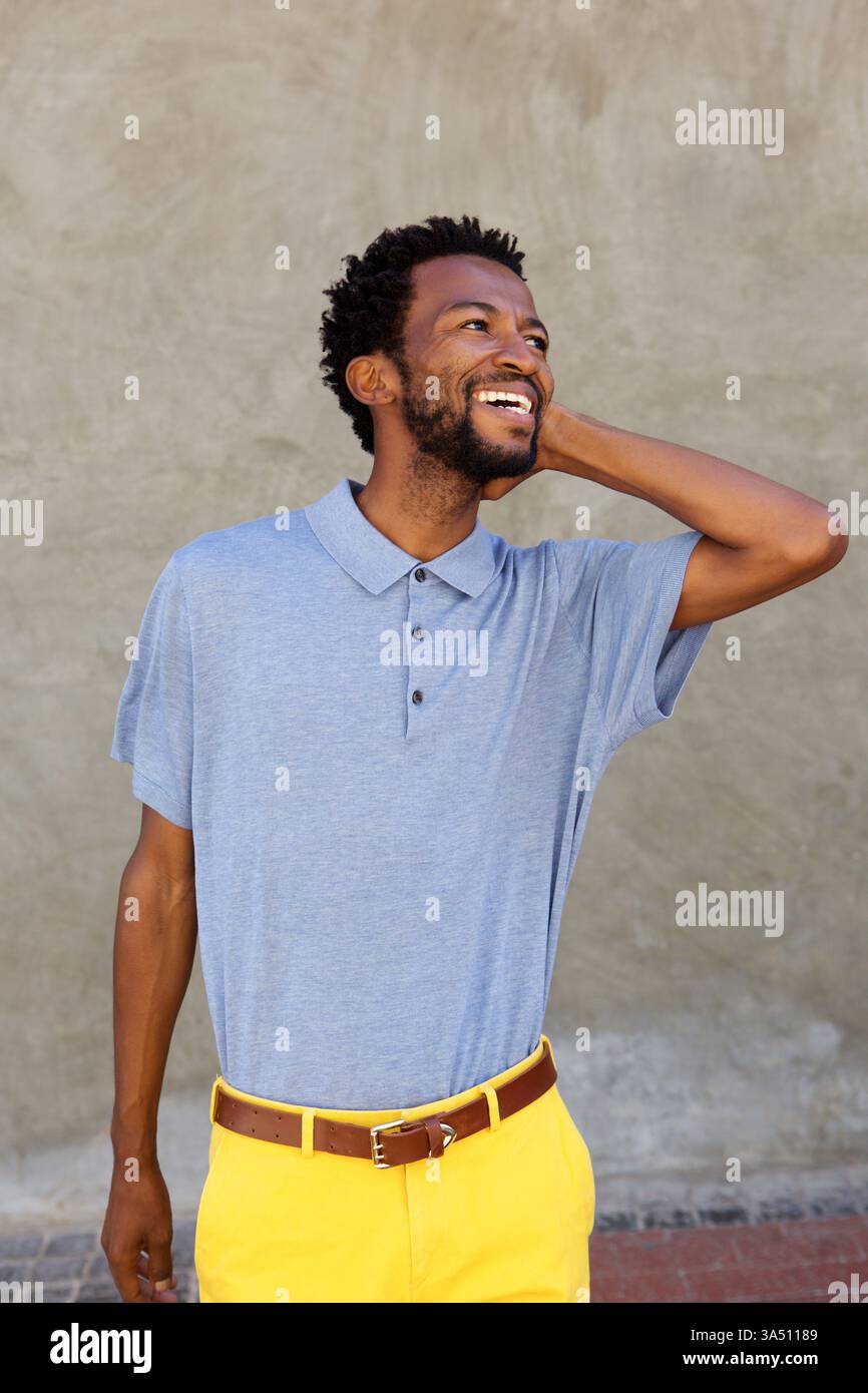 Portrait d'un homme insouciant et attrayant souriant avec sa main posée sur sa tête. Une image de style de vie décontracté qui communique confiance, positivité et style moderne. Convient pour la mode, l'image de marque personnelle et les campagnes de style de vie. Banque D'Images