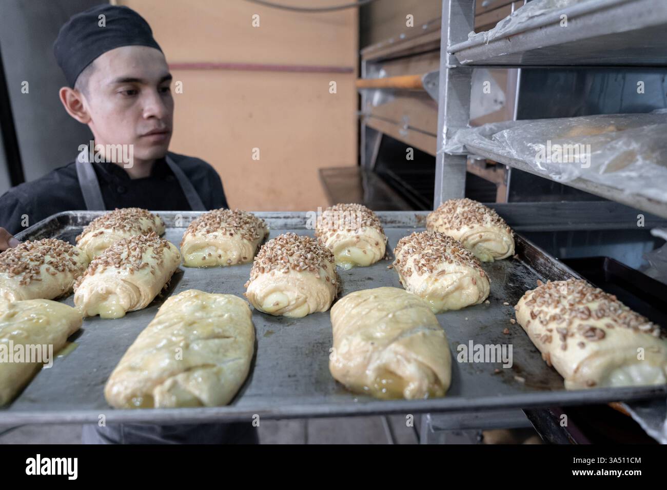 Boulanger hispanique sélection d'un plateau de pains à pâtisserie sur les étagères pour cuire au four. Scène de boulangerie intérieure chaleureuse présentant des bonbons mexicains traditionnels et des pâtisseries faites à la main. Idéal pour la boulangerie, l'industrie alimentaire et les campagnes de cuisine culturelle. Banque D'Images