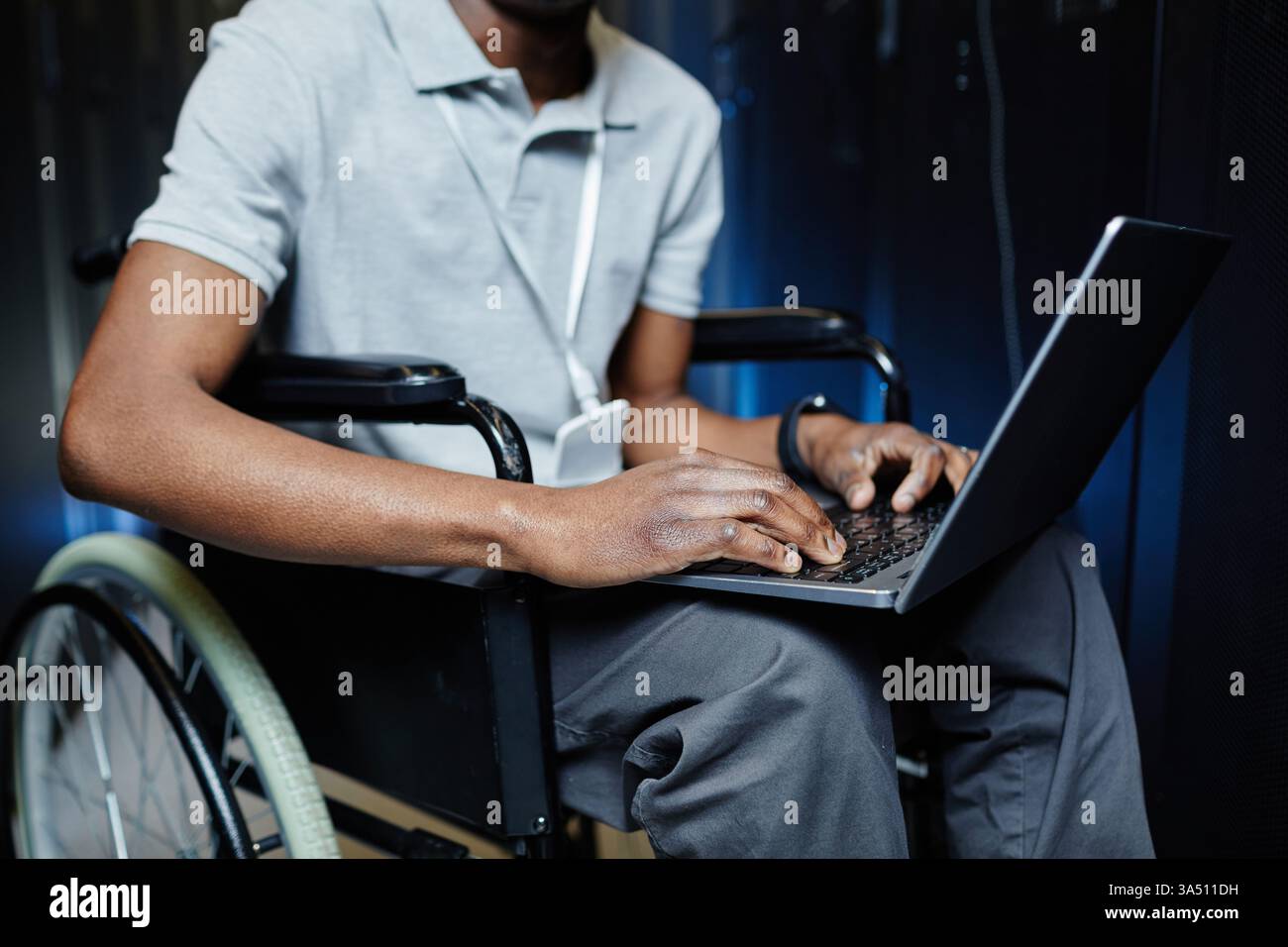 Gros plan d'un technicien INFORMATIQUE noir handicapé utilisant un ordinateur portable dans une salle de serveurs. Met l'accent sur l'accessibilité dans les environnements technologiques, INFORMATIQUES et de datacenter. Convient aux thèmes de l'espace de travail inclusif et de la technologie d'assistance. Banque D'Images