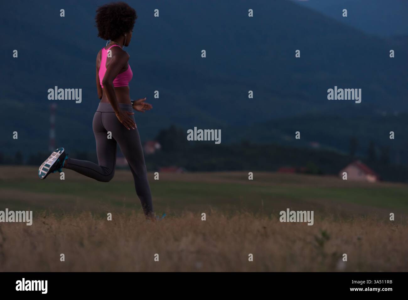 Jeune femme afro-américaine faisant du jogging en plein air dans la nature avec des écouteurs lors d'une nuit d'été. Cette image de fitness est idéale pour le bien-être, le style de vie actif et les campagnes sportives. Banque D'Images