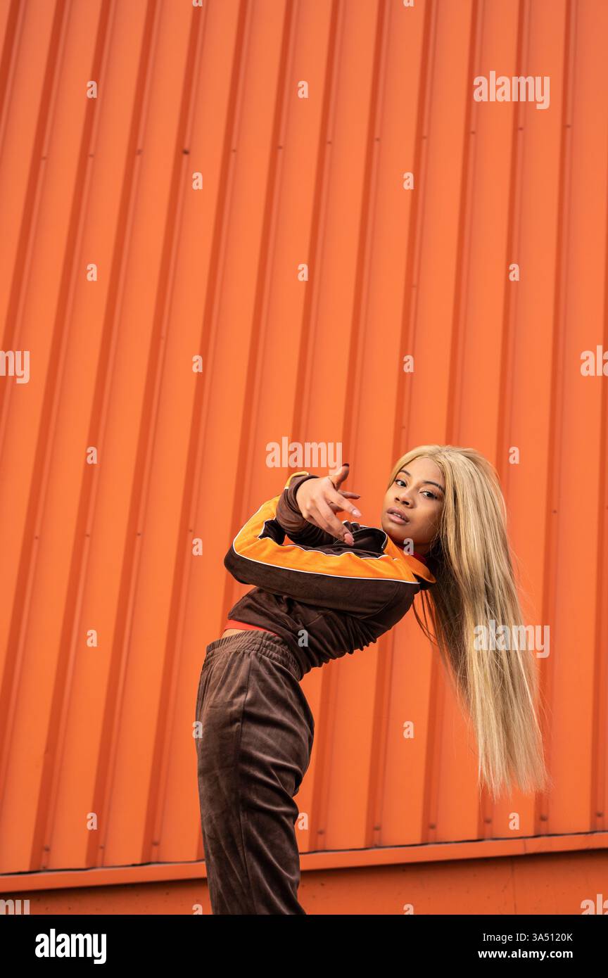 Heureuse jeune femme en vêtements de sport dansant dans une rue de la ville. Son mouvement énergique et ses vêtements d'athlétisme brillants s'adaptent au fitness, au style de vie et aux campagnes de mode de rue. Parfait pour les magazines, les marques promouvant la vie active, le style de jeunesse et l'énergie urbaine. Banque D'Images