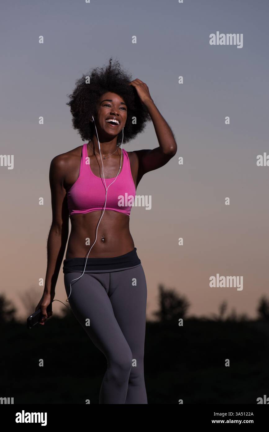 Jeune femme noire en bonne santé s'étire après le jogging lors d'une belle soirée d'été dans la nature. L'image transmet la vitalité et la vie saine pour les campagnes de fitness et de bien-être, l'entraînement en plein air et les paysages de parc. Banque D'Images