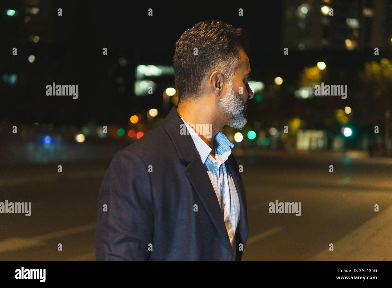 Vue latérale d'un homme d'affaires sérieux portant des vêtements élégants debout contre des lampes incandescentes et regardant loin à l'heure du soir dehors Banque D'Images