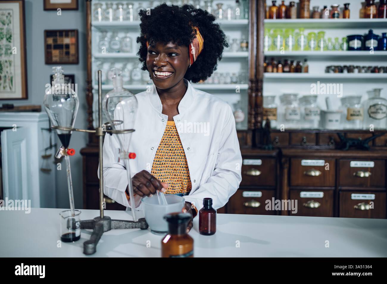 Joyeux chimiste afro-américain dans une apothicaire vintage mélange un composé dans un mortier et un pilon. Un portrait sur le thème de la santé et de la pharmacie. Banque D'Images