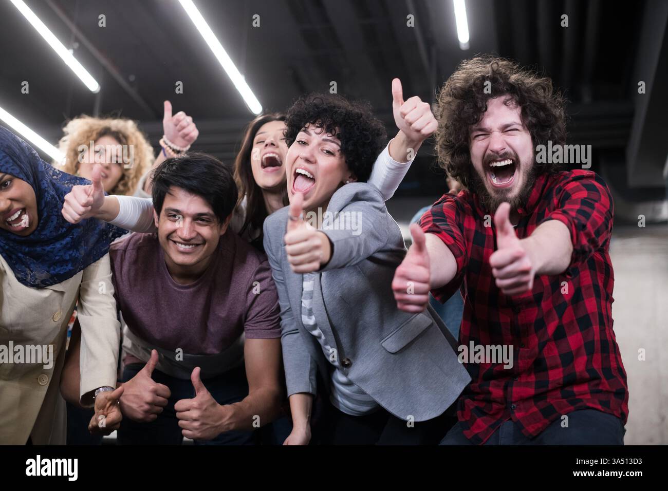 Un groupe diversifié de développeurs de logiciels célèbrent le succès dans un bureau de démarrage moderne. L'équipe enthousiaste se tient ensemble, regardant la caméra, incarnant le travail d'équipe et l'esprit d'entreprise. Parfait pour les visuels professionnels et technologiques mettant en valeur la diversité, la collaboration et la réussite. Banque D'Images