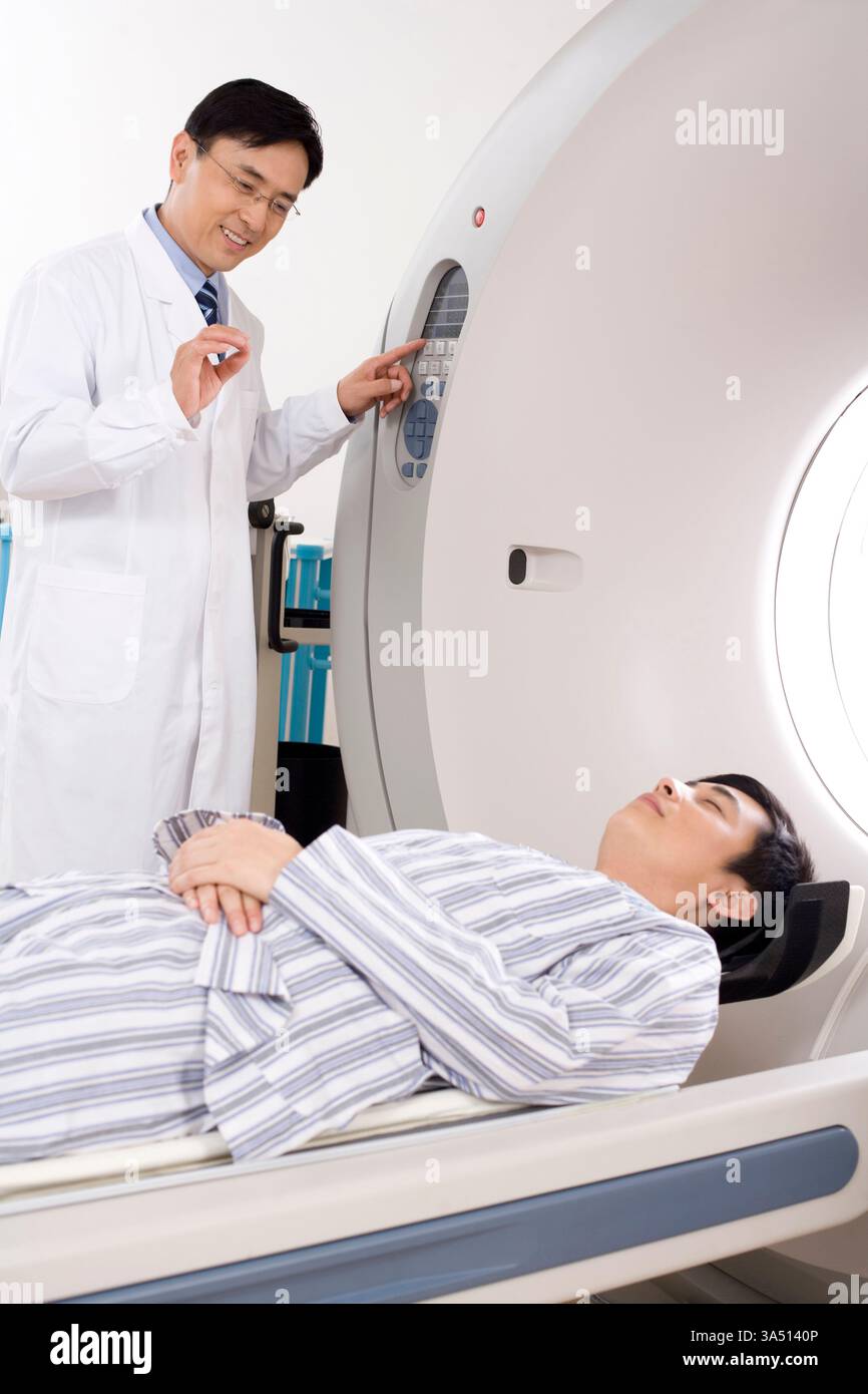 Médecin chinois aidant un patient dans un scanner IRM. L'imagerie médicale et la radiologie sont représentées dans un cadre clinique. Cette scène met en lumière les soins, les procédures diagnostiques et les professionnels de la santé. Banque D'Images