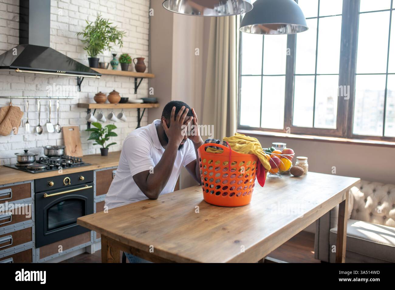 Homme noir avec expression malheureuse assis à table avec panier à linge à l'intérieur Banque D'Images