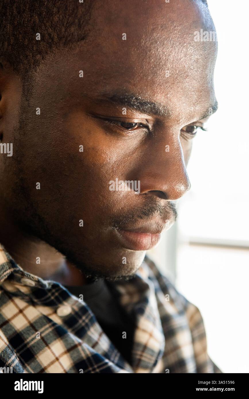 Gros plan portrait latéral d'un homme afro-américain avec une expression réfléchie et focalisée. Ce headshot est adapté aux portraits, aux caractéristiques de style de vie et à la marque personnelle. Banque D'Images