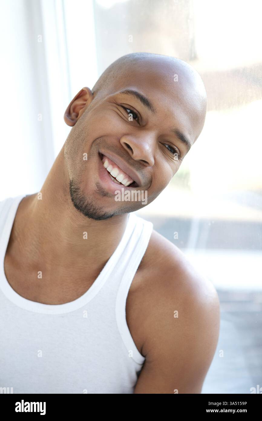 Portrait en gros plan d'un jeune homme heureux souriant et regardant par une fenêtre. Cette image chaleureuse de style de vie convient à la vie quotidienne, à la confiance et à la vie urbaine. Idéal pour les campagnes de marque, de mode et de style personnel. Banque D'Images