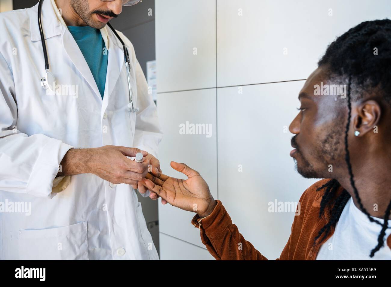 Un professionnel de la santé teste le taux de sucre dans le sang d'un jeune homme dans une clinique moderne. Cette image des soins de santé met l'accent sur le diagnostic et la surveillance de conditions telles que l'hypoglycémie en soins primaires. Banque D'Images