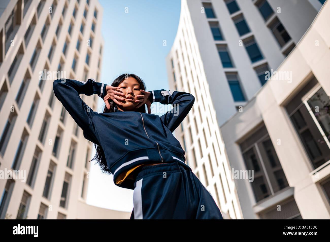 Jeune femme asiatique en tenue athlétique marche le long d'une rue urbaine entourée de bâtiments. La scène convient aux campagnes de fitness en plein air et de style de vie actif. Banque D'Images
