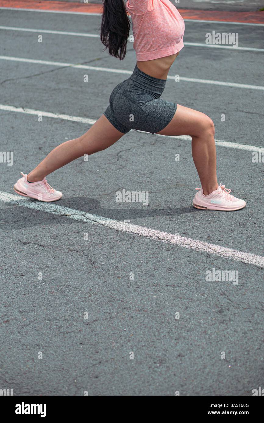 Un athlète hispanique sans visage en tenue athlétique effectue la pose Virabhadrasana Warrior sur une piste de course de stade. La vue latérale met l'accent sur l'équilibre, la force et la forme physique en plein air pendant l'entraînement. Banque D'Images