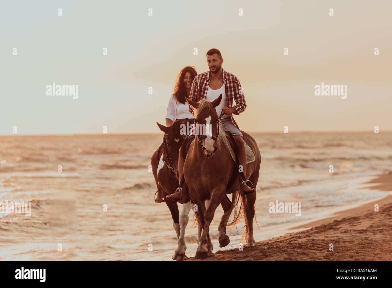 Un couple aimant en vêtements d'été monte un cheval sur une plage de sable au coucher du soleil. La scène présente la mer, la lumière chaude et un moment romantique en plein air. Banque D'Images