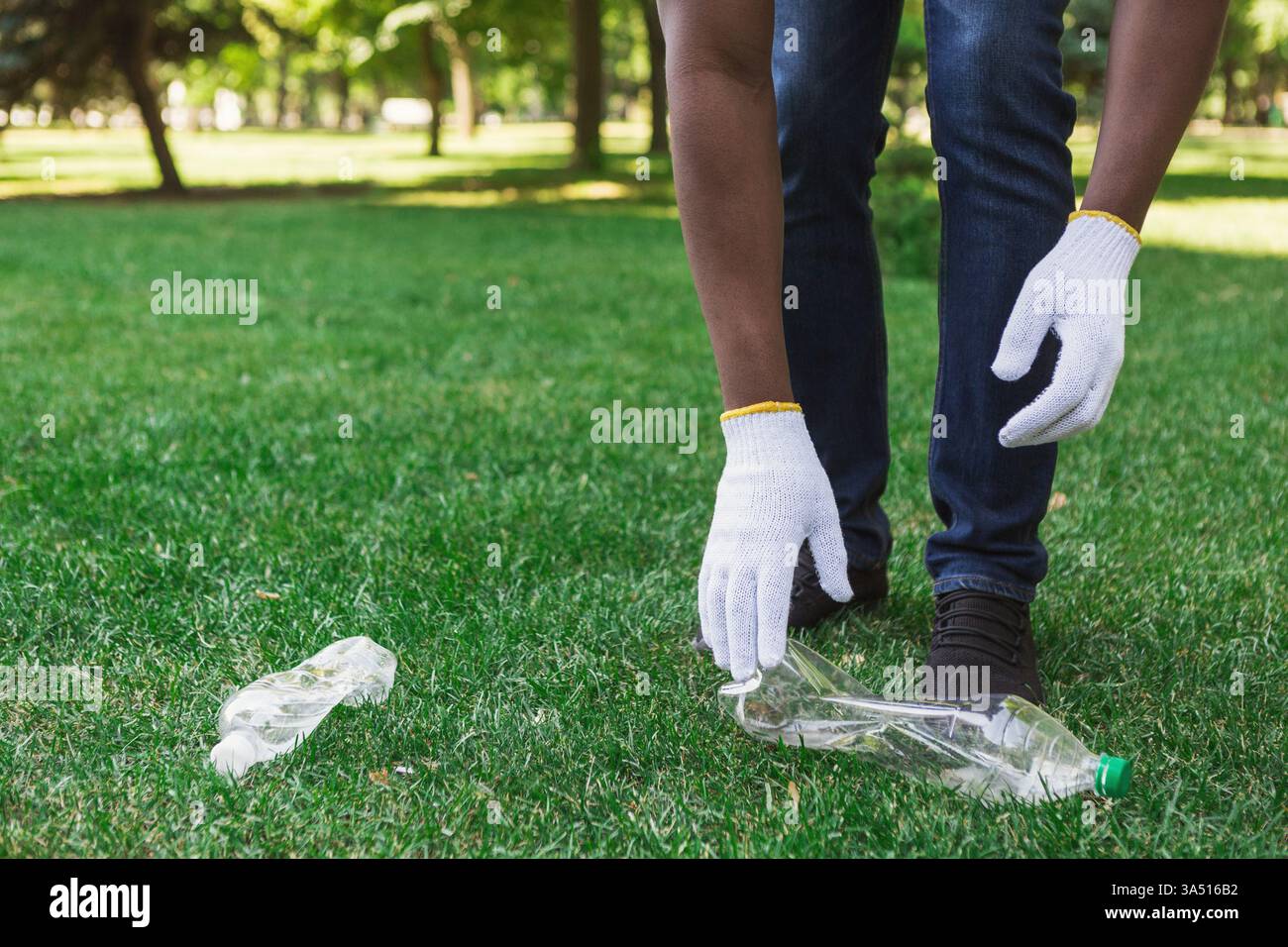 Un homme noir collecte une bouteille en plastique pour la recycler dans un parc, mettant en avant le bénévolat et l'action écologique. Cette scène extérieure met l'accent sur le nettoyage de l'environnement, la réduction des déchets et les soins communautaires. Idéal pour les campagnes sur les programmes de recyclage, la durabilité et la responsabilité sociale. Banque D'Images