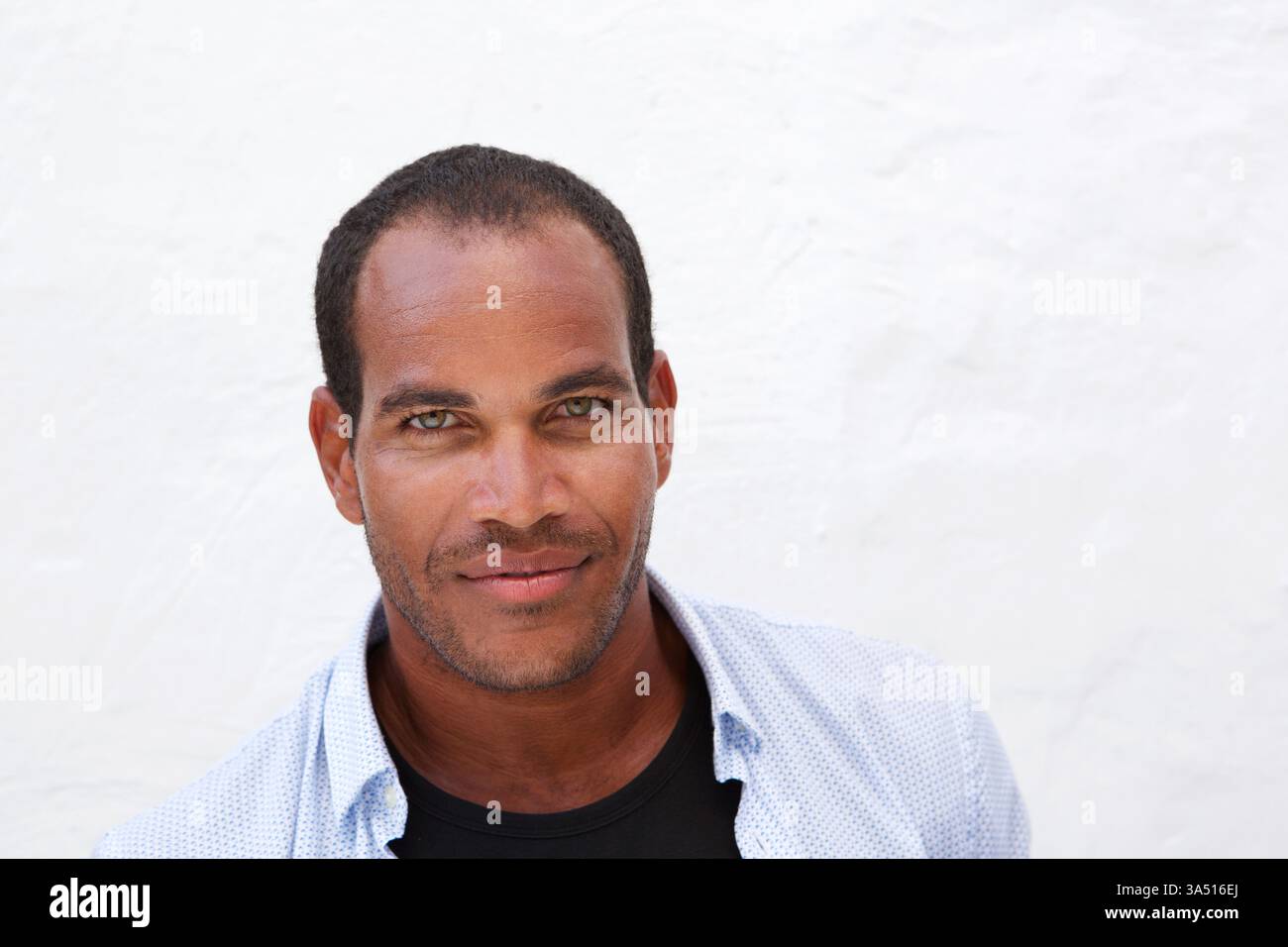Un homme hispanique se tient contre un mur blanc dans un portrait moderne. L'image transmet confiance et style, adapté aux campagnes de marque personnelle et de style de vie. Une option polyvalente pour les portraits masculins et les études de personnages contemporains. Banque D'Images