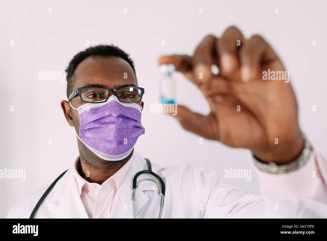 Médecin masculin noir dans un masque médical montre une dose de vaccin, favorisant la vaccination et la santé publique. Le milieu professionnel soutient les campagnes de soins de santé, l'éducation médicale et les communications hospitalières. Banque D'Images