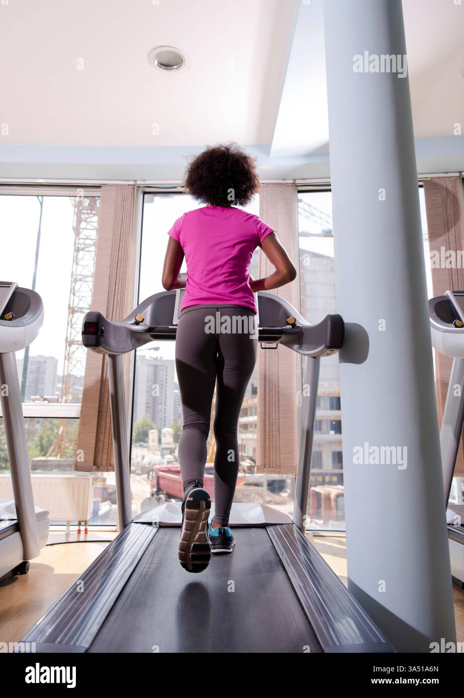 Femme noire avec un afro portant des vêtements de fitness court sur un tapis roulant à la salle de gym pendant la journée. Une image dynamique pour les campagnes de fitness, d'entraînement et de vie saine. Banque D'Images