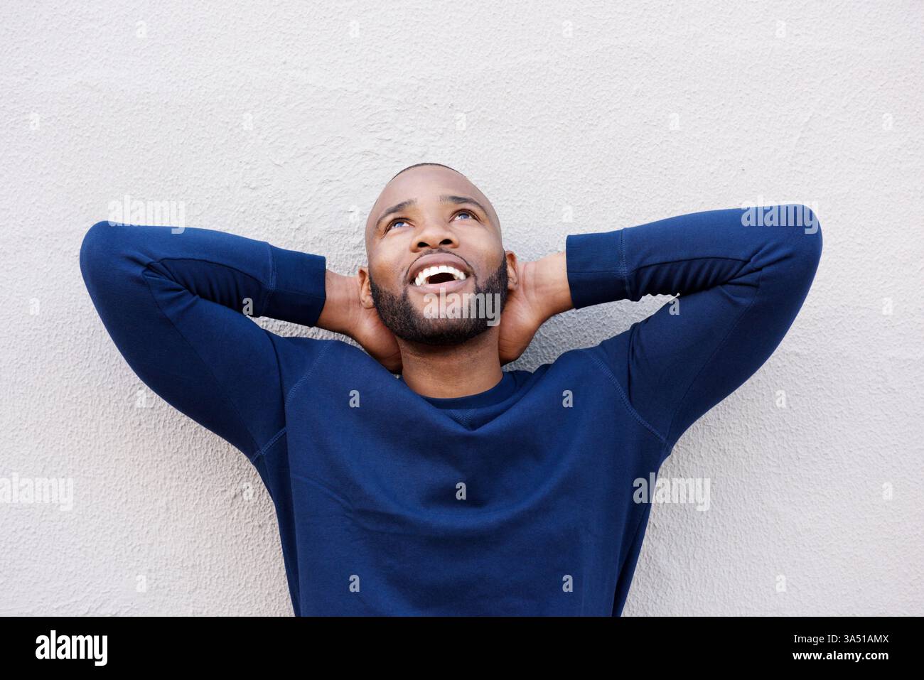 Gros plan portrait d'un homme confiant debout, les mains derrière la tête, regardant vers le haut. Cette photo de style de vie décontracté transmet positivité, confiance et style moderne. Idéal pour l'épanouissement personnel, la motivation et l'imagerie masculine contemporaine. Banque D'Images
