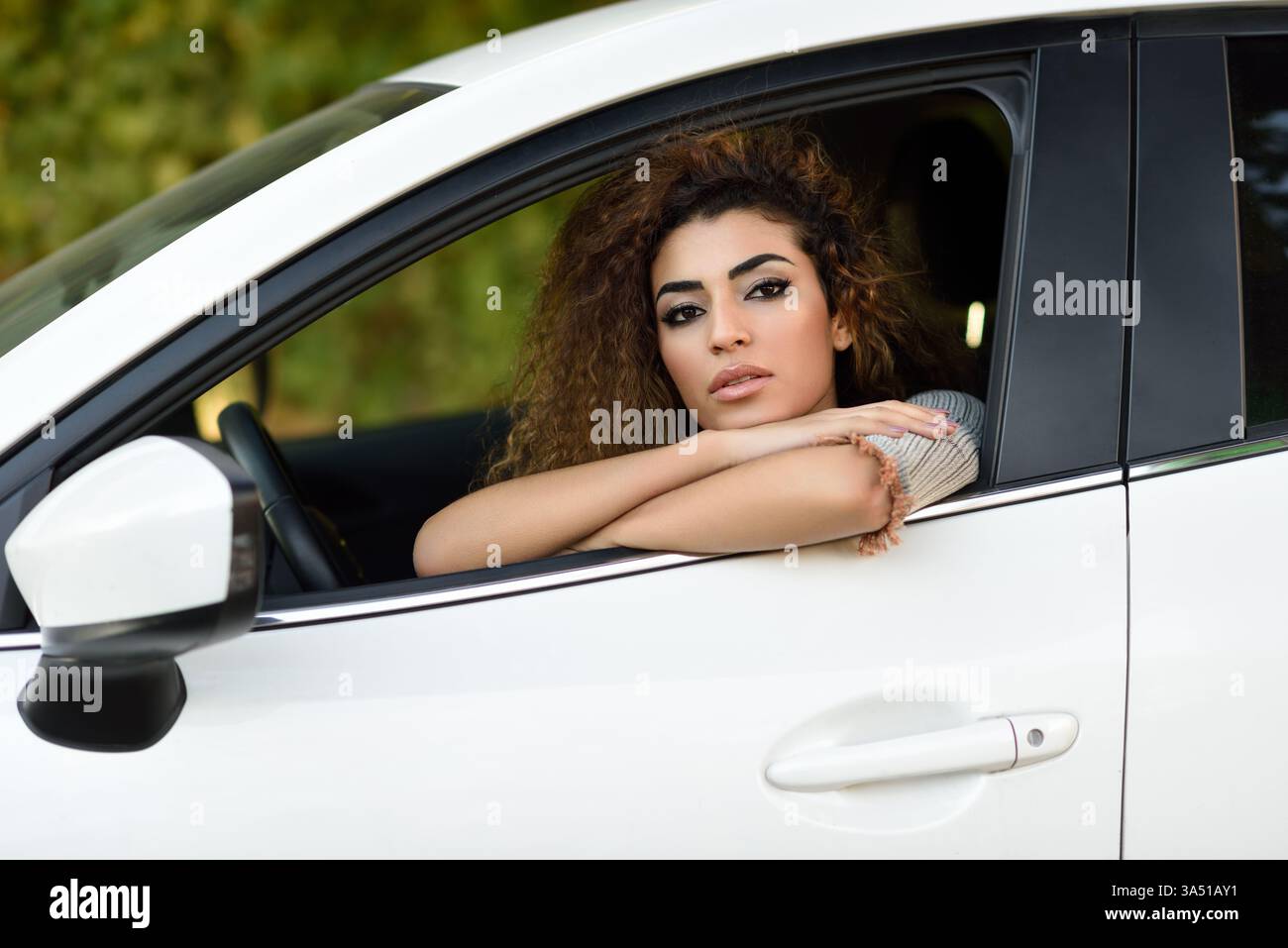 Belle jeune femme du moyen-Orient assise dans une voiture blanche, regardant par la fenêtre. Images de style de vie urbain et décontracté adaptées aux voyages, à la conduite automobile et aux thèmes de l'automobile. Idéal pour les visuels automobiles et contemporains mettant en vedette une femme arabe moderne. Banque D'Images