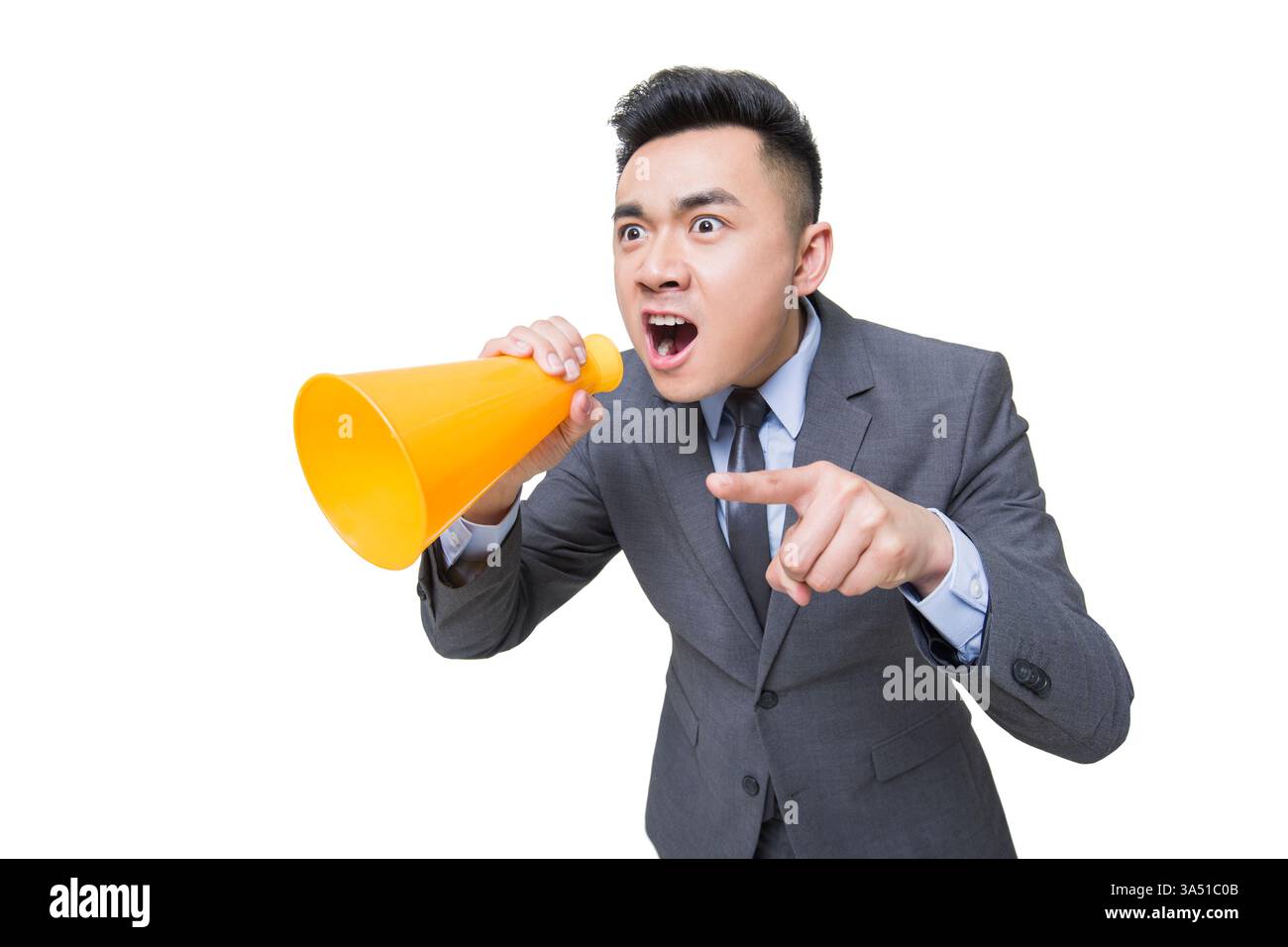 Un homme d'affaires chinois en colère crie dans un mégaphone, faisant des gestes avec un doigt pointu. Cette image de studio utilise un fond blanc propre pour mettre l'accent sur le pouvoir, l'urgence et la confrontation dans un contexte commercial. Idéal pour des sujets tels que la politique de bureau, la pression de leadership, ou la résolution de problèmes sur le lieu de travail. Banque D'Images