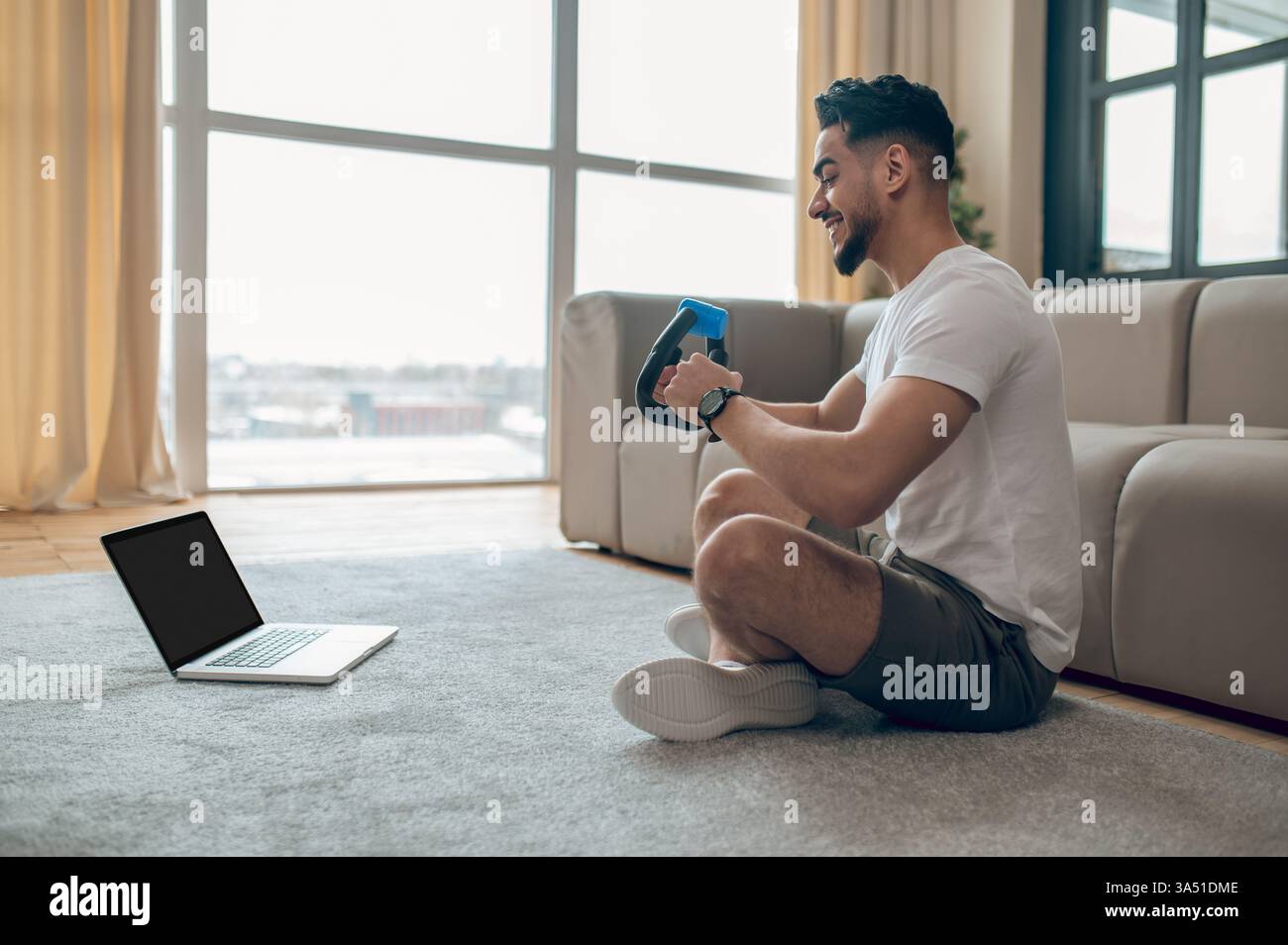 Jeune homme effectuant un entraînement à domicile avec un expandeur dans un cadre intérieur lumineux. Cette image de style de vie de fitness convient aux articles sur rester actif, les routines de gymnastique à domicile et les entraînements en ligne. Parfait pour les campagnes de bien-être et de vie saine. Banque D'Images