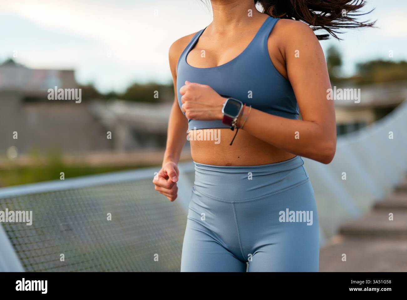 Femme latino-américaine concentrée dans le jogging sportswear dans un environnement urbain avec une smartwatch. Idéal pour les campagnes de fitness, de bien-être et de technologie portable. Image dynamique pour les entraînements en ville et la vie active. Banque D'Images