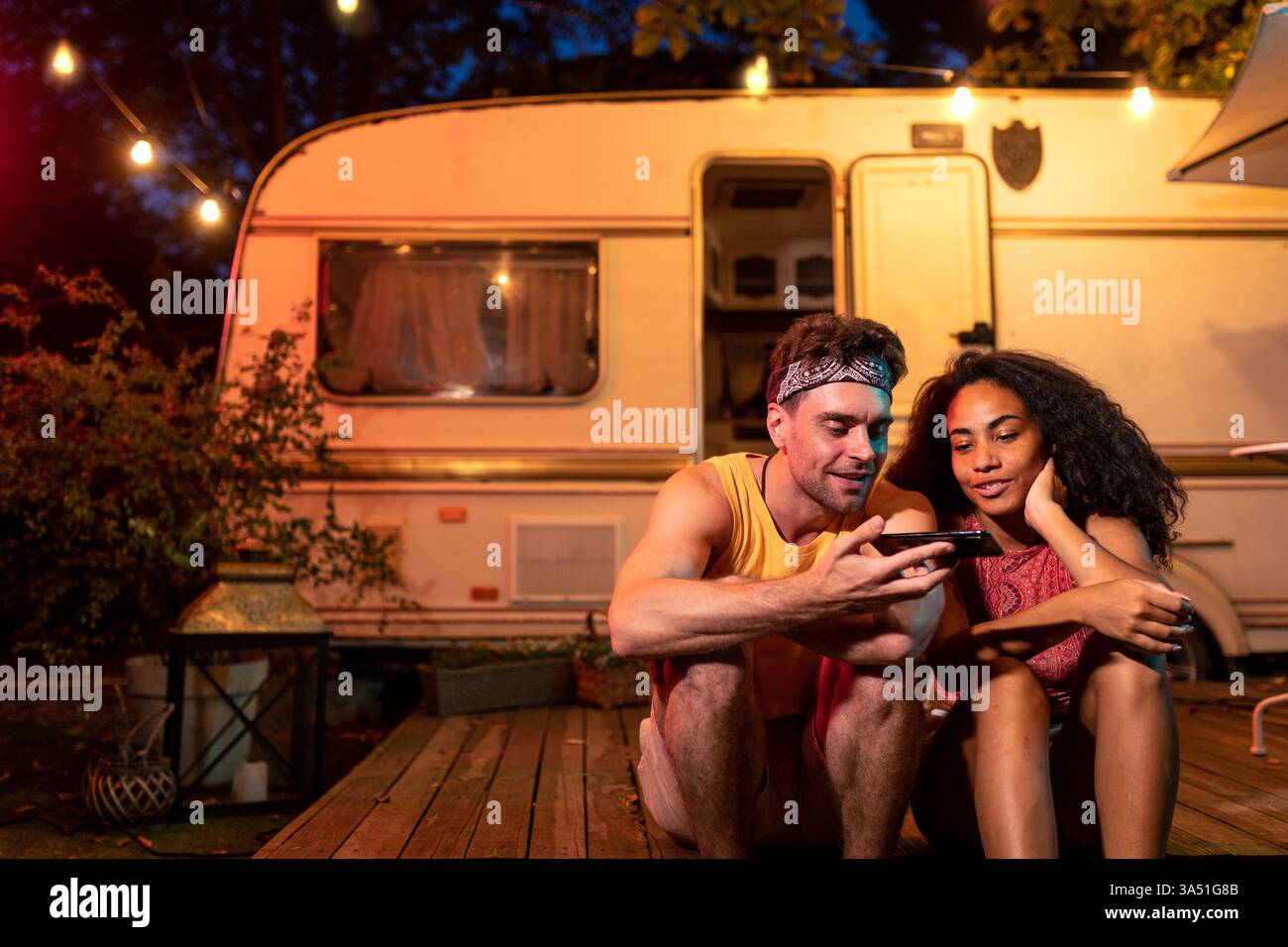 Jeune couple en vacances à côté d'un camping-car, profitant d'une nuit dans la nature. Une scène inspirée de la wanderlust parfaite pour les voyages en voiture, le camping et les thèmes de style de vie en plein air. Idéal pour les voyages, les couples et le marketing d'aventure. Banque D'Images