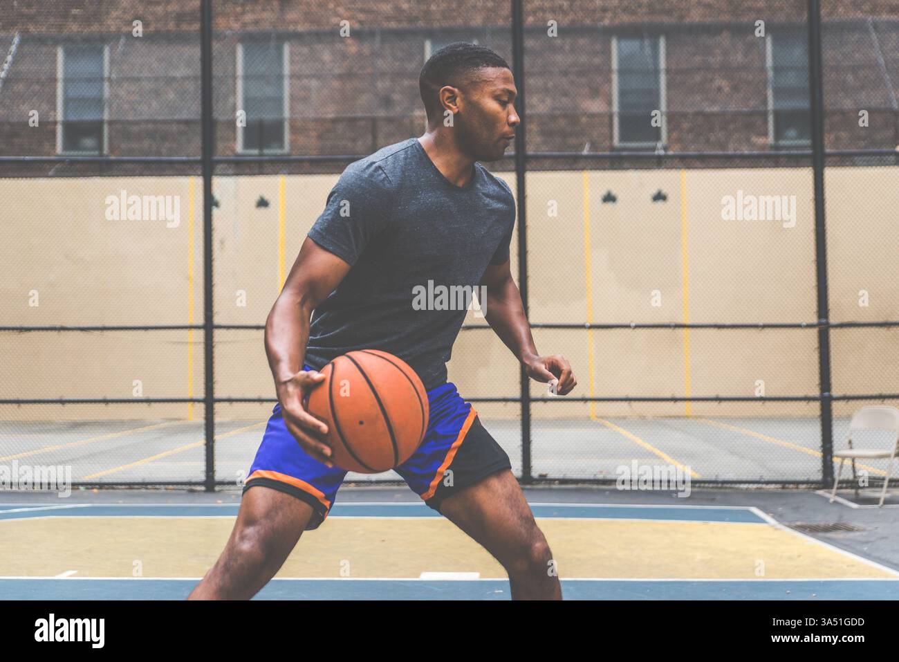 Un aspirant joueur de basket-ball s'entraîne sur un court de New York, capturé dans un environnement sportif urbain dynamique. L'image met l'accent sur le dévouement, l'entraînement et la poursuite d'objectifs dans le basket-ball, parfait pour les sports, le streetball et les campagnes de style de vie urbain. Idéal pour les portraits d'athlètes et les contextes de gymnastique ou d'entraînement. Banque D'Images