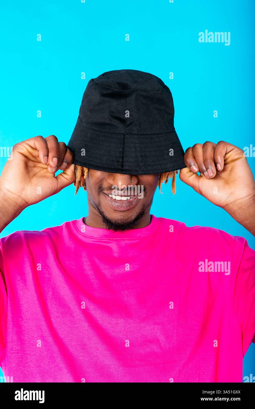 Homme hispanique souriant avec un chapeau sur un fond de studio bleu vif. Ce portrait est décontracté et convivial, adapté à la mode, au style de vie et aux images marketing. Une image polyvalente pour un style personnel et une image de marque positive. Banque D'Images