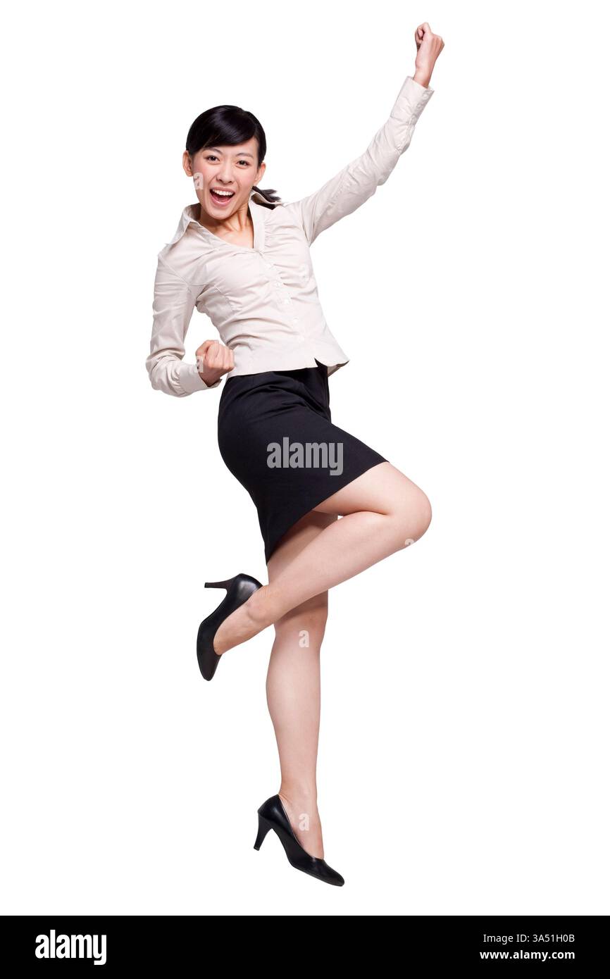 Femme d'affaires chinoise excitée sautant avec les bras levés dans un cadre de studio. Cette image dynamique exprime la réussite, la motivation et l'énergie positive pour les communications d'entreprise. Banque D'Images