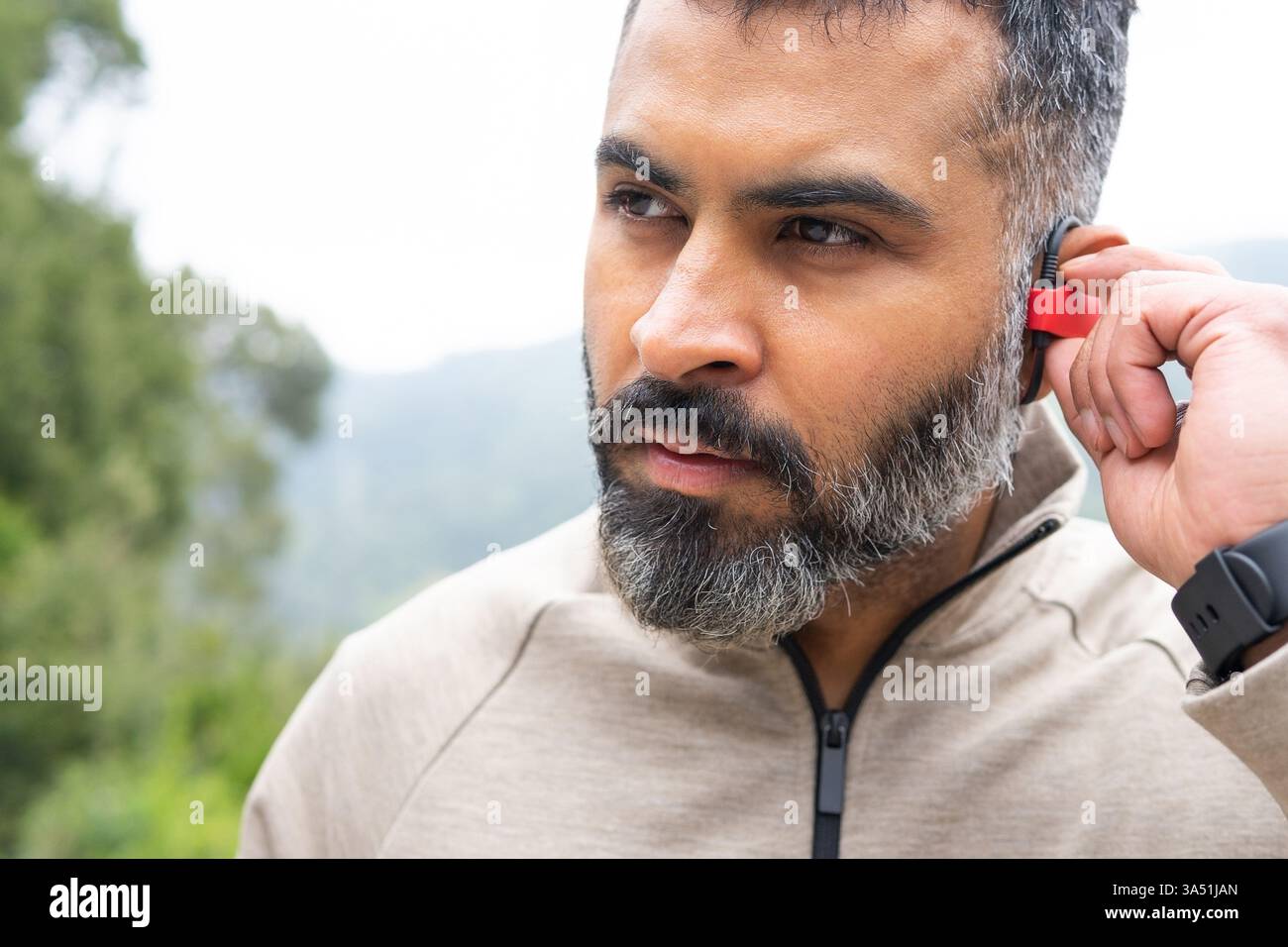 Portrait d'un homme barbu en tenue sportive allumant des écouteurs sans fil. Convient pour les scènes de fitness, de course et de bien-être avec un style de vie actif. Banque D'Images