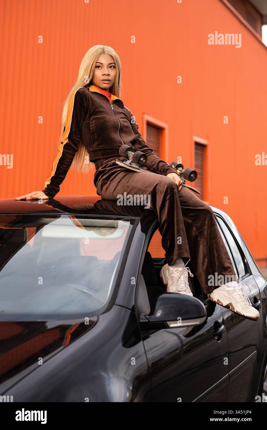 Jeune femme noire avec de longs cheveux blonds en tenue athlétique pose sur un fond orange. Une image de style de vie et de fitness audacieuse parfaite pour les campagnes de vêtements de sport et les thèmes de vie active. Banque D'Images