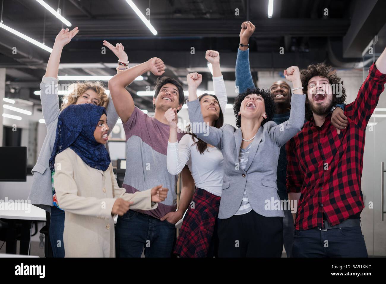 Équipe de développement de logiciels multiethniques célébrant le succès dans un bureau de démarrage moderne. Ils se tiennent ensemble, regardant la caméra avec des sourires, transmettant le travail d'équipe et la réussite. Idéal pour les images professionnelles, technologiques et culturelles d'entreprise. Banque D'Images