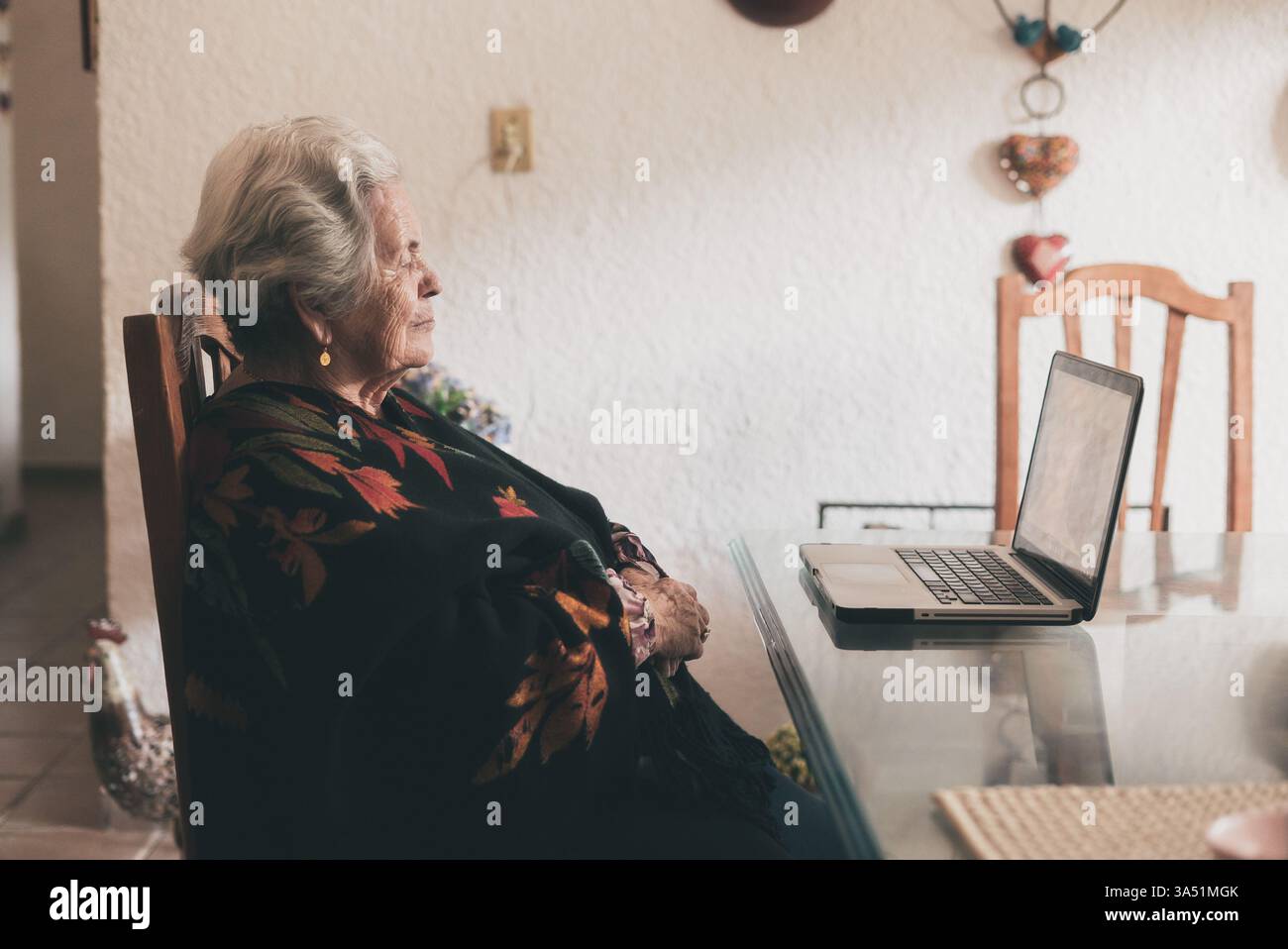 Femme hispanique senior chat vidéo sur un ordinateur portable à la maison. Ambiance chaleureuse de bureau à domicile illustrant la communication à distance et le fait de rester connecté. Idéal pour le style de vie des seniors, le télétravail et l'imagerie numérique d'inclusion. Banque D'Images