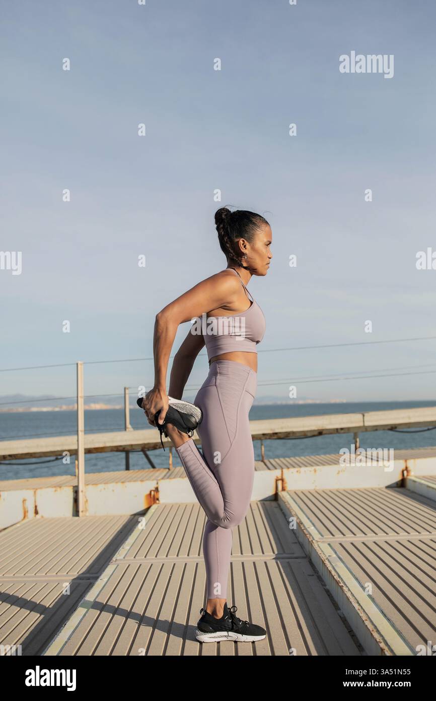 Une femme afro-américaine en vêtements d'activité s'étire sur un escalier en remblai, mettant en évidence le fitness et l'entraînement en plein air. La photo lumineuse et énergique convient à la photographie de bien-être, de gymnastique et de style de vie qui met l'accent sur le mouvement et la vitalité. Banque D'Images
