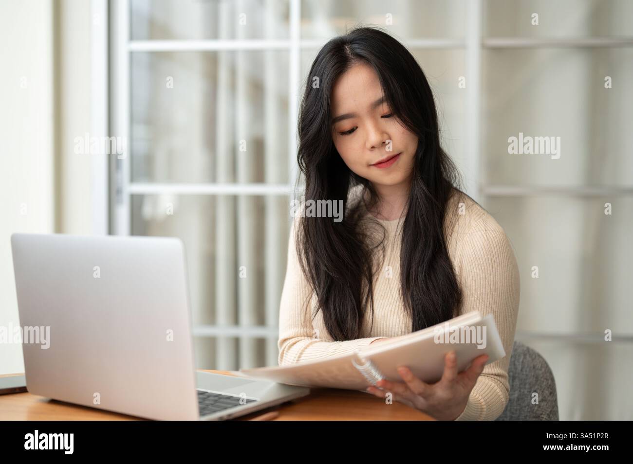 Femme asiatique sérieuse lisant des notes assis à table avec ordinateur portable à la maison Banque D'Images