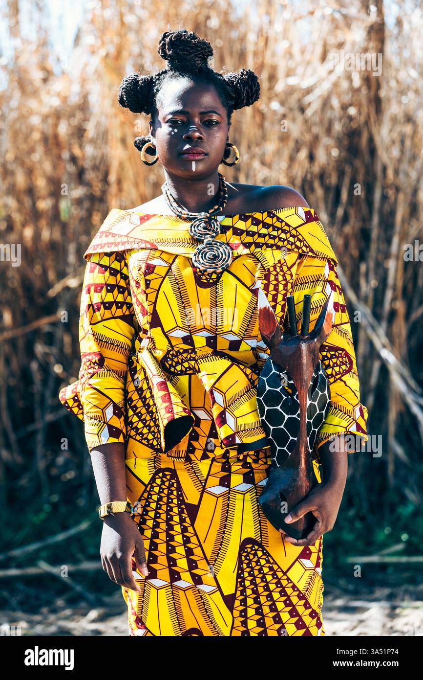 Femme noire avec des brioches de cheveux se tient dans un champ ensoleillé parmi de grandes herbes sèches. Un portrait en plein air vibrant mettant l'accent sur la culture, la mode et la lumière naturelle. Convient pour les campagnes de style de vie ou ethnique. Banque D'Images