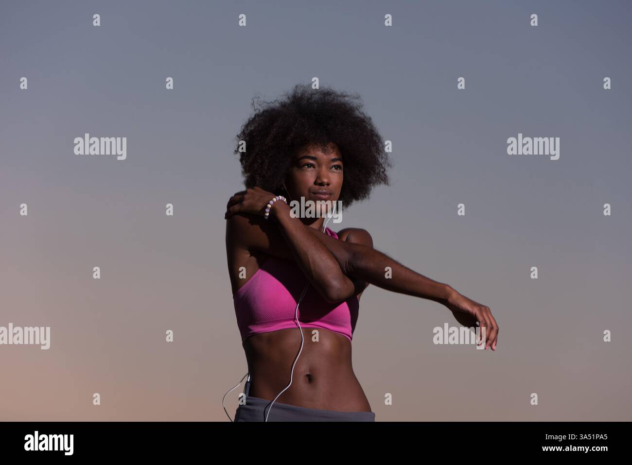 Jeune femme noire en bonne santé effectuant un échauffement d'étirement après un jogging dans un pré à l'heure dorée. Parfait pour le fitness, le bien-être, les activités de plein air et les campagnes de style de vie estivales. Le cadre naturel et la lumière douce en font un accessoire idéal pour les visuels sur le thème de la santé et de la motivation. Banque D'Images