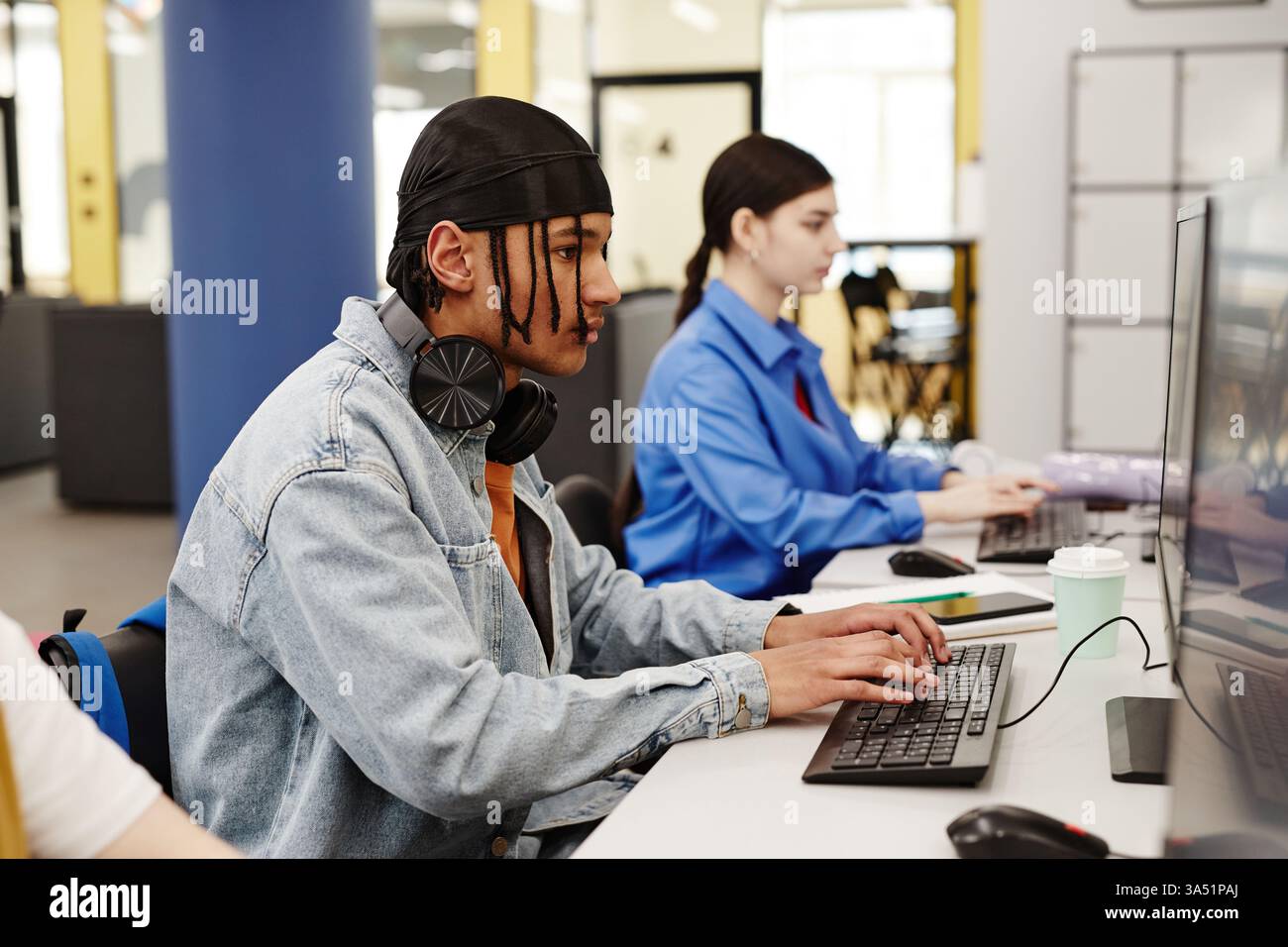 Étudiants masculins et féminins de race mixte utilisant un ordinateur assis à la table faisant des recherches dans la bibliothèque Banque D'Images