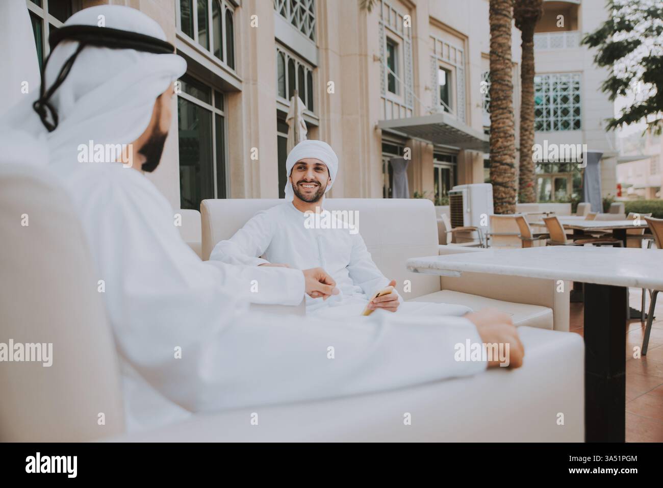 Deux jeunes hommes d'affaires de Dubaï portent des tenues traditionnelles de kandura alors qu'ils marchent le long de la Marina. Le cadre urbain allie affaires et loisirs dans un environnement moderne du Golfe. Idéal pour les articles sur la culture d'entreprise du moyen-Orient, le réseautage et les marchés régionaux. Banque D'Images