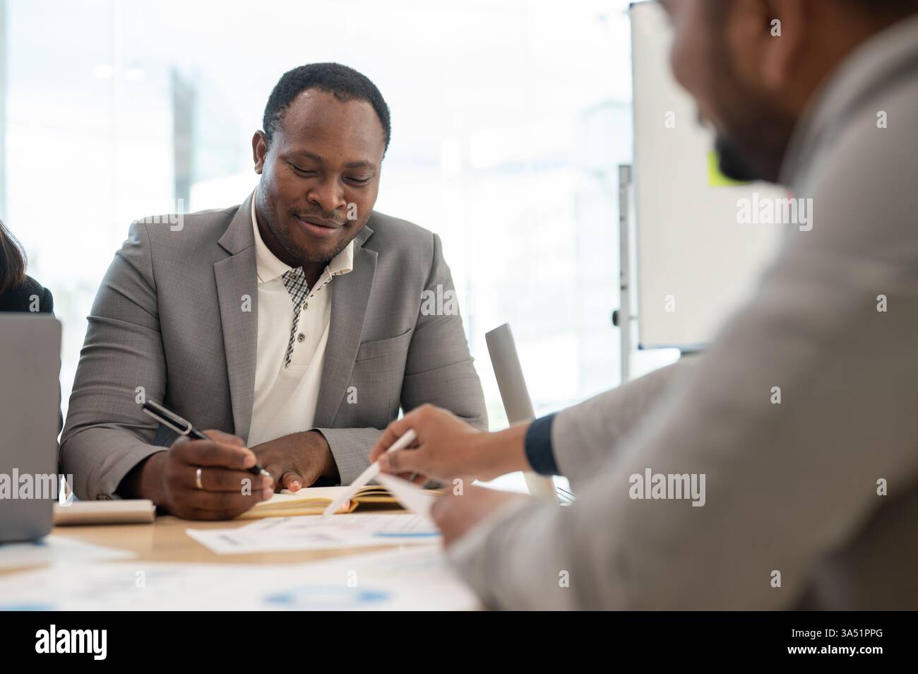 Souriant Noir et Indien hommes d'affaires ayant une réunion tout en étant assis à table dans le bureau Banque D'Images