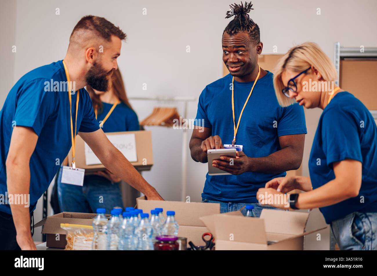 Groupe multiracial de volontaires dans un centre caritatif, collaborant aux efforts de secours. Un Afro-américain travaille avec des collègues pour emballer des dons et organiser des fournitures. Cette scène d’équipe diversifiée met en valeur le travail d’équipe, le bénévolat et le soutien communautaire. Banque D'Images
