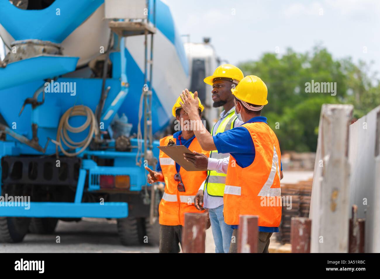 Foreman dirige une équipe sur un chantier de construction, planifiant le projet avec les travailleurs et les ingénieurs. Un malaxeur de camion à béton et un équipement sur site mettent en évidence la gestion active du site. Idéal pour les visuels de l'industrie de la construction, la supervision de site ou la narration d'ingénierie. Banque D'Images